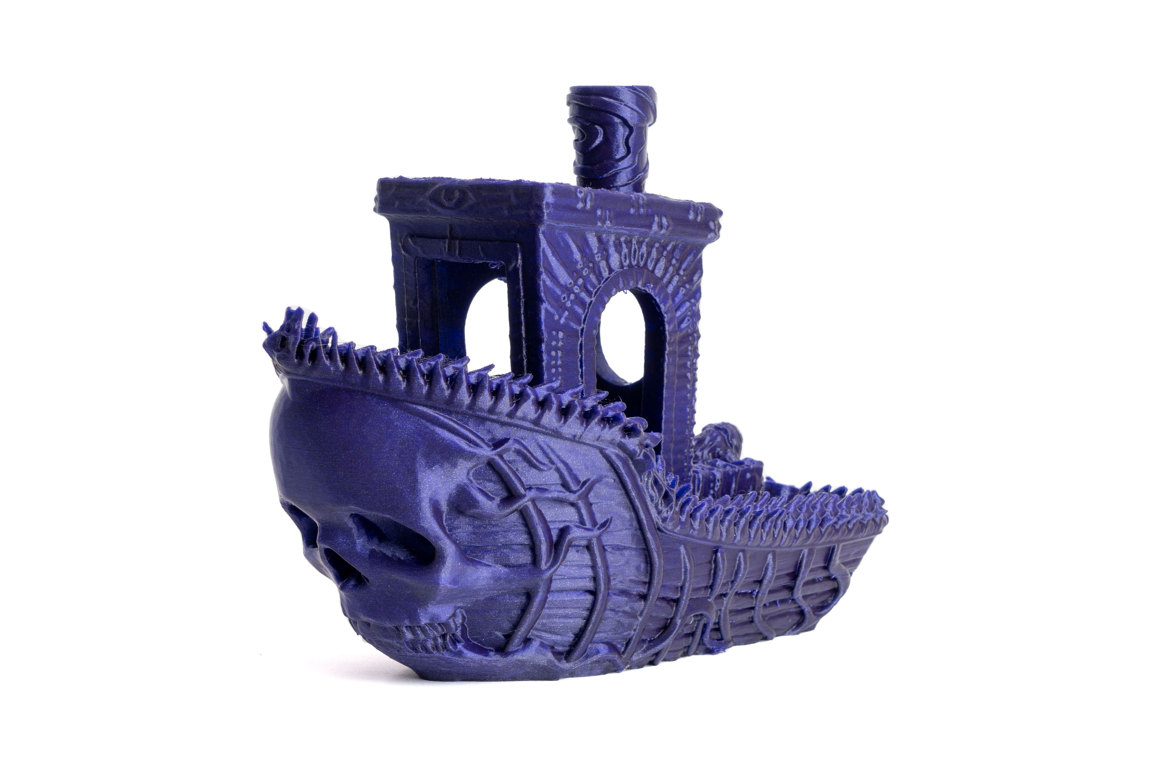 A 3D-printed model resembling a boat with an intricate skull design on the front. The surface is made of a shiny dark purple material with detailed textures, such as ribbed lines a