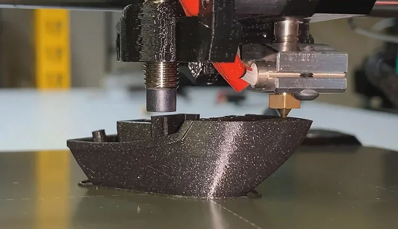 Prusa Mini 3D printer nozzle creating detailed black boat model with precise layers on build plate, showcasing print quality and design capability.