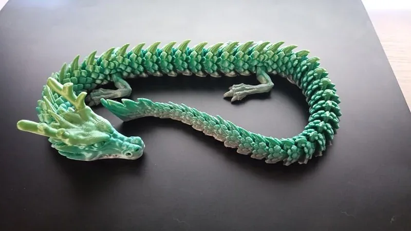 Flexible dragon model created by Prusa Mini 3D printer, showcasing intricate details, green scales, and articulated design on a dark surface.