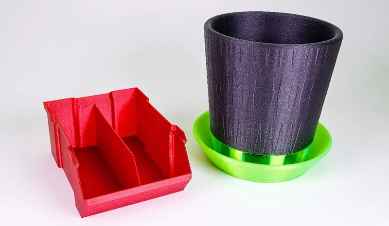 Prusa Mini 3D prints include a red organizer and a black pot with a green base, showcasing diverse object creation capabilities.