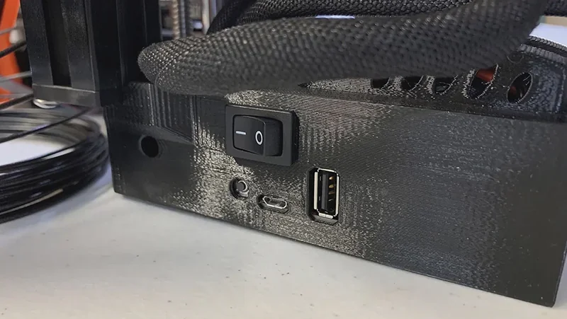 Prusa Mini 3D printer power switch and ports, including USB and micro-USB, with black braided cables on a white surface.