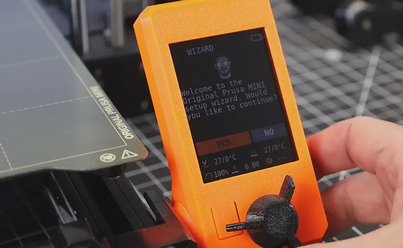 Prusa Mini 3D printer's setup screen showing wizard prompt, orange casing, and Original Prusa branding on print bed corner.