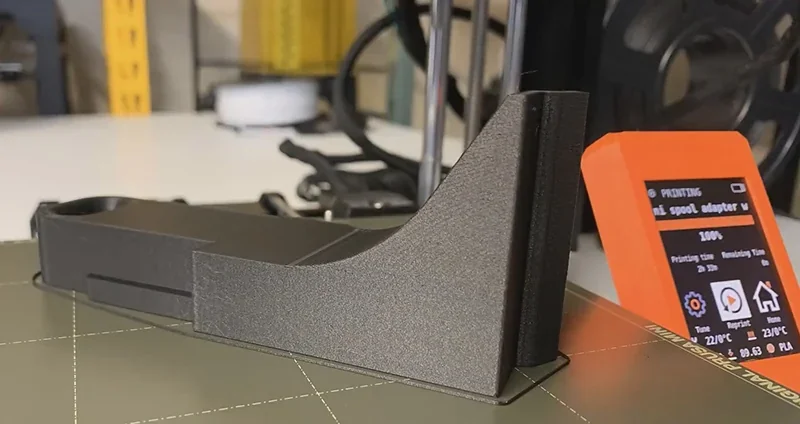 Prusa Mini 3D printer with printed part and digital display, showcasing precision and functionality in a workshop setting.