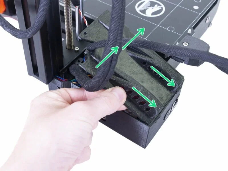 Prusa Mini 3D printer wiring setup, a hand adjusts a cable cover with arrows indicating cable management, showcasing efficient organization.