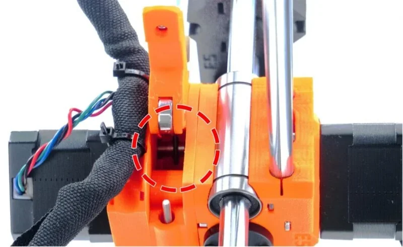 Close-up of a Prusa Mini 3D printer's orange extruder assembly with highlighted metal part, showing wiring and mechanical components.