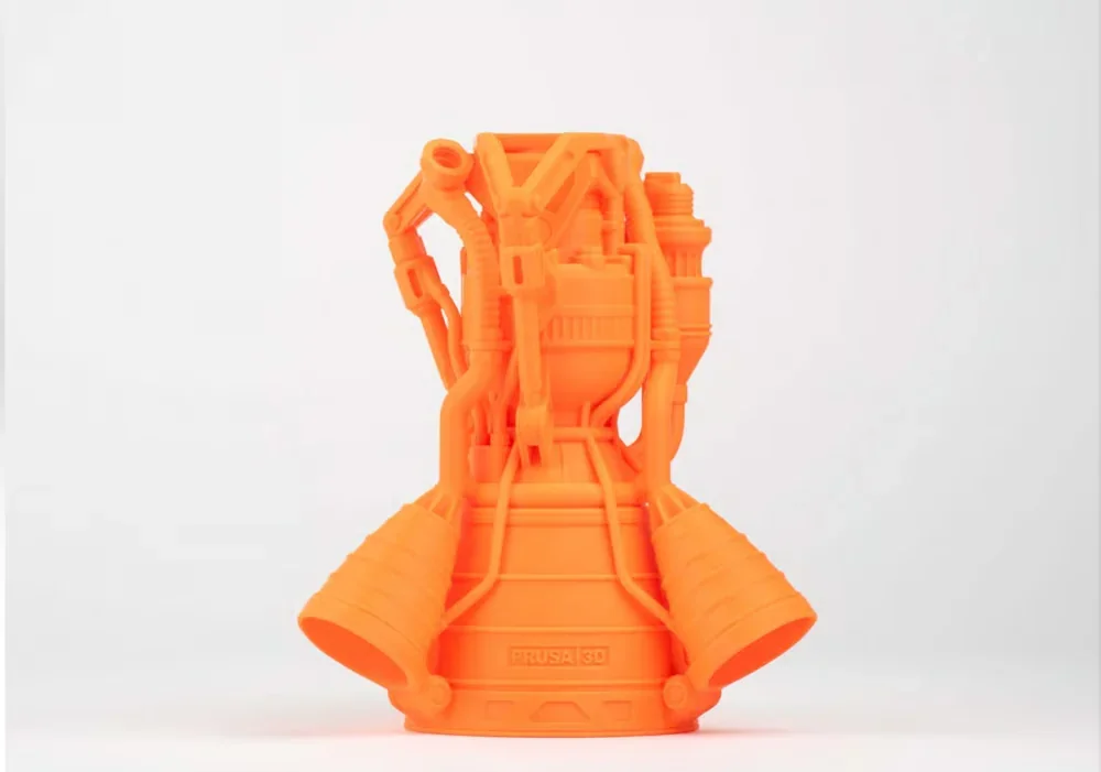 Orange 3D-printed engine model showcasing intricate details, created by Prusa MK4 printer, with "Prusa 3D" branding visible on base.