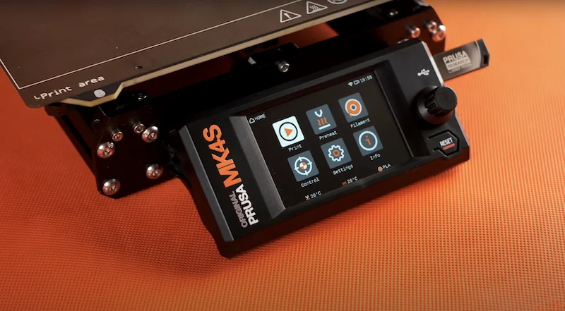 Prusa MK4 3D printer display panel with control knobs and branding, set on an orange surface; print samples likely created by the printer.