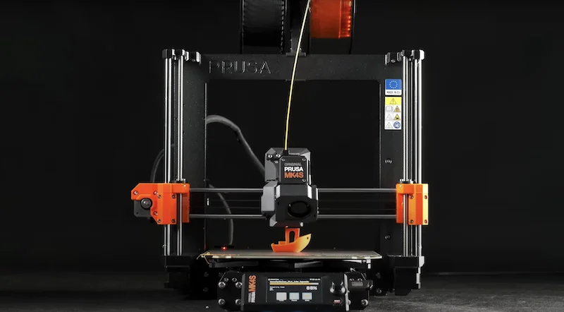 Prusa MK4 3D printer with orange accents printing a yellow part, featuring a touchscreen interface and branding on a dark background.