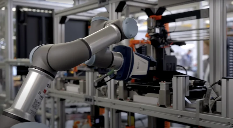 Industrial Prusa MK4 3D printer with robotic arm in a modern factory setting, showcasing automation and precision manufacturing.