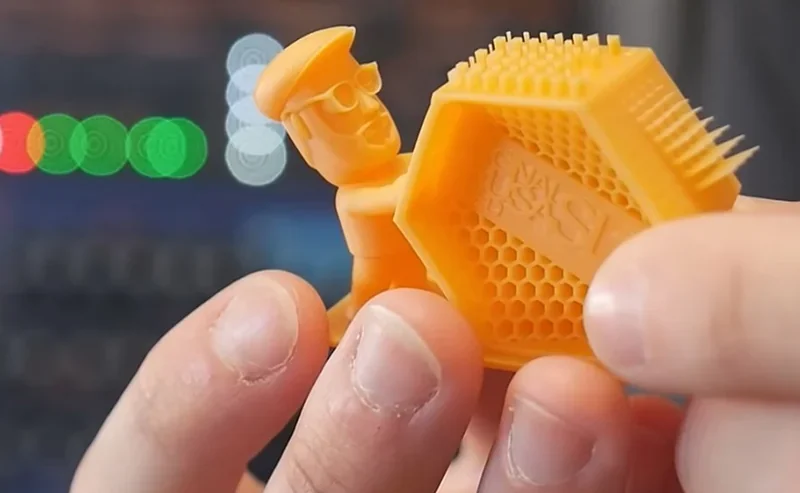 Prusa SL1S printed model held in hands, showing detailed yellow 3D figurine with a honeycomb pattern hexagon object, close-up view.