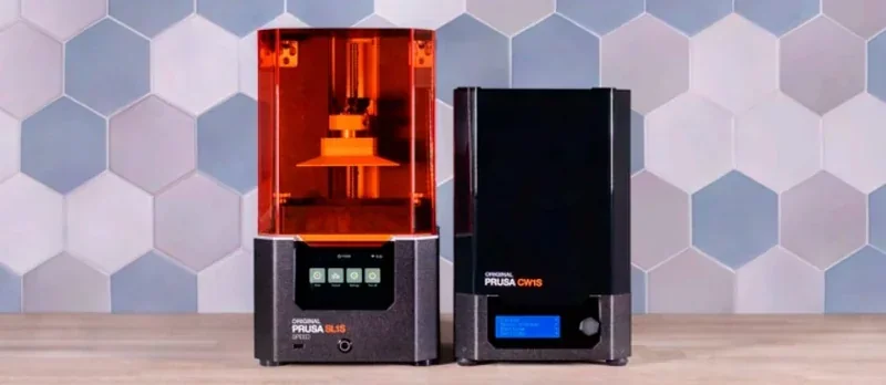 Prusa SL1S and CW1S on a wooden surface, hexagonal tiled background, featuring orange cover and touchscreen display.