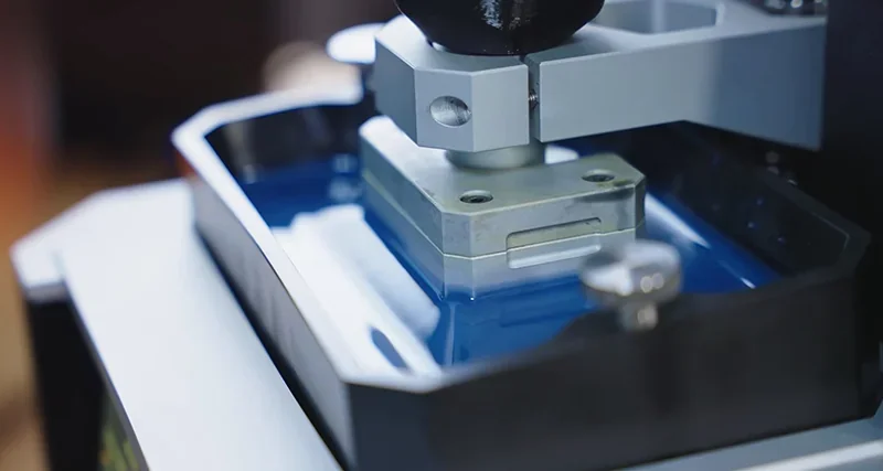 Prusa SL1S 3D printer in action, showcasing a metal component being printed in resin, highlighting precision and technology.