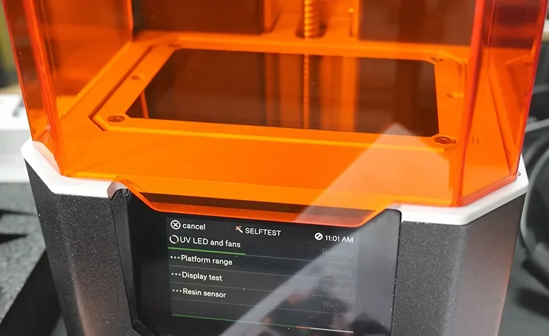 Prusa SL1S 3D printer with orange cover, display showing self-test and resin sensor, indicating samples made by this printer model.