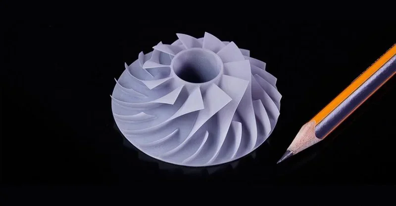 Prusa SL1S-printed turbine model beside a pencil on a black background, showcasing precision detail and scale comparison.