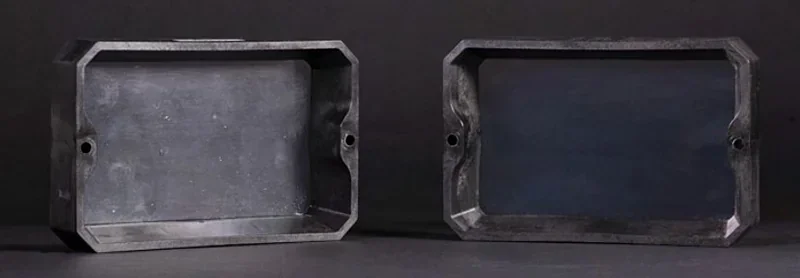 Prusa SL1S-created two rectangular black 3D-printed parts with beveled edges and screw holes, shown on a dark surface.