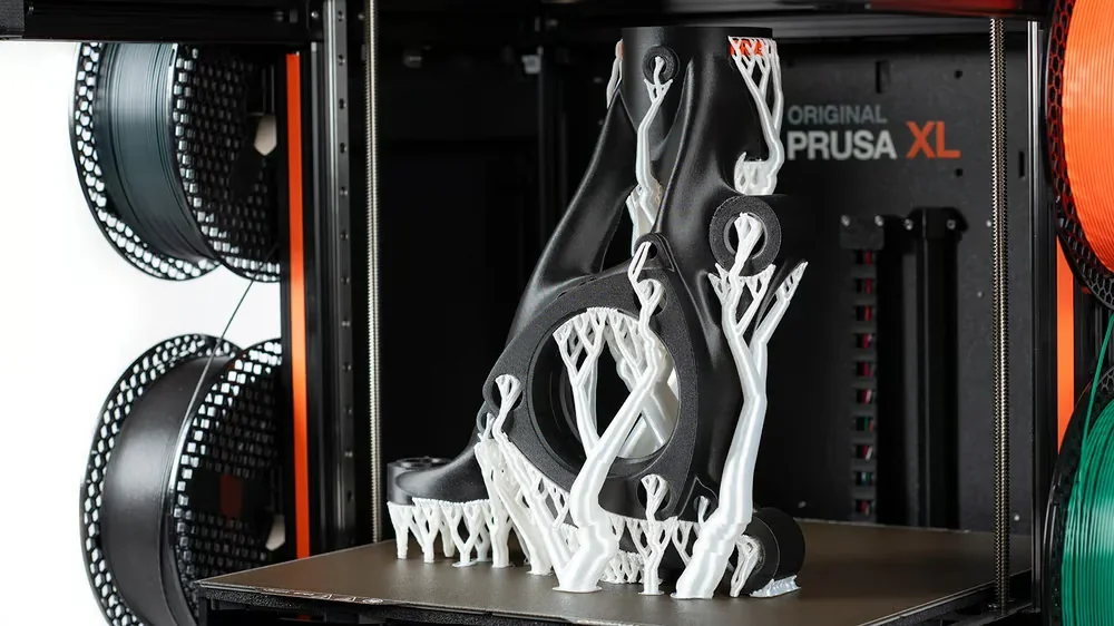 Prusa XL 3D printer showcasing a complex black and white model with visible spools and branding in a production setting.