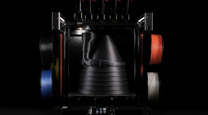 Prusa XL 3D printer with multi-color filament spools produces large black cone-shaped part in dark setting.