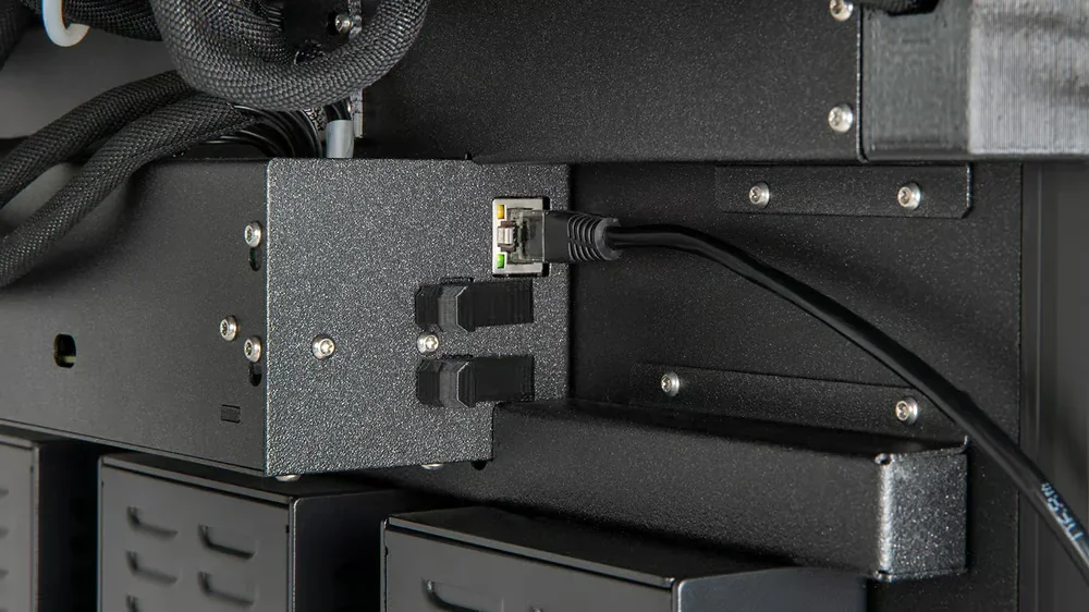 Prusa XL 3D printer close-up showing networking components with Ethernet cable and sleek black finish.