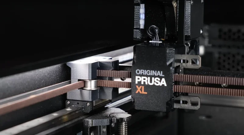 Prusa XL 3D printer with visible belt and detailed components, showcasing precision engineering in a sleek, modern design.