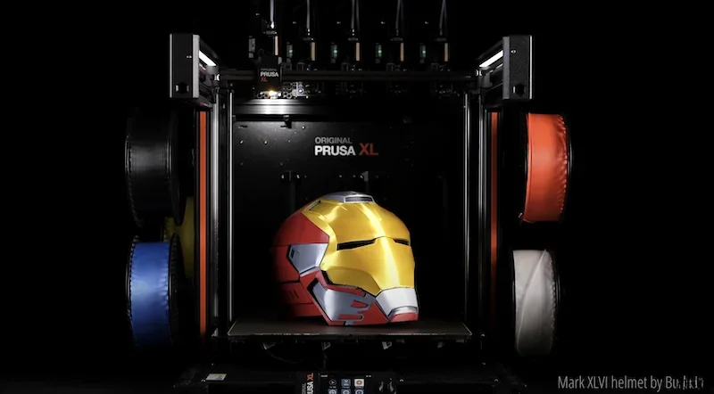 Prusa XL 3D printer displaying a completed multicolored Iron Man helmet print, with filament spools visible on sides.