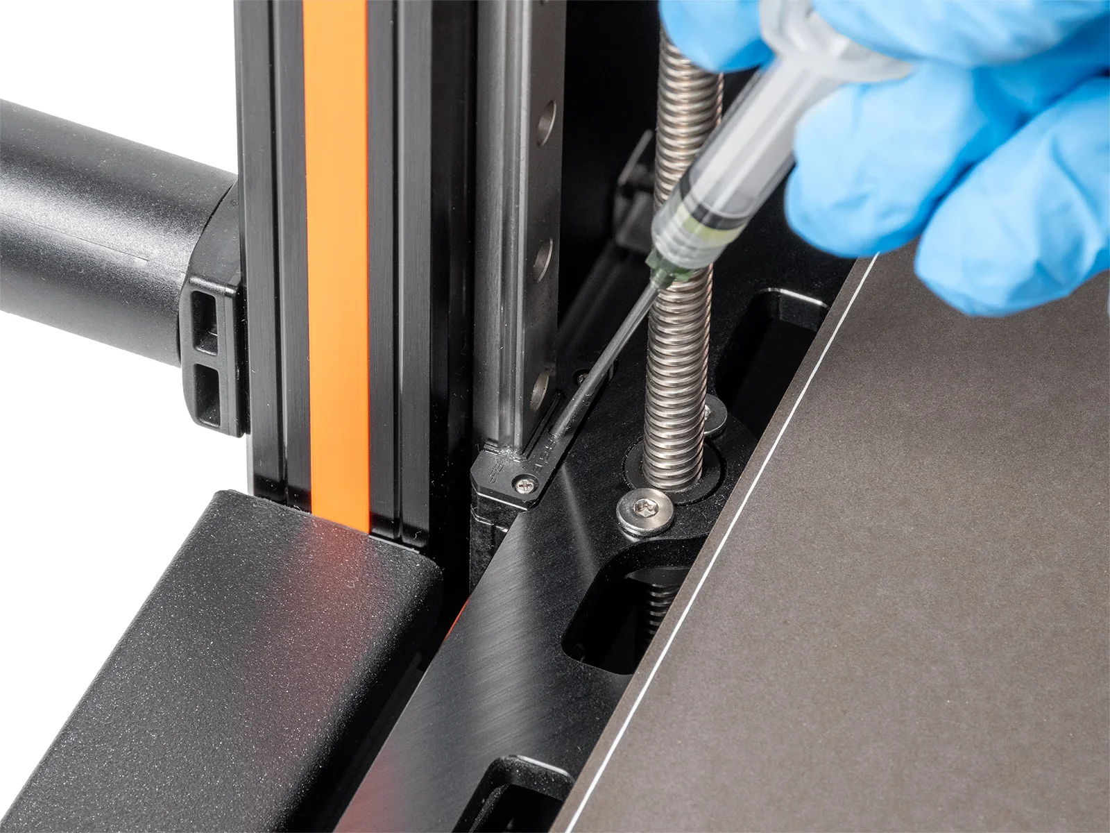 Gloved hand lubricating Prusa XL 3D printer's threaded rod, showing parts and maintenance process in close-up detail.