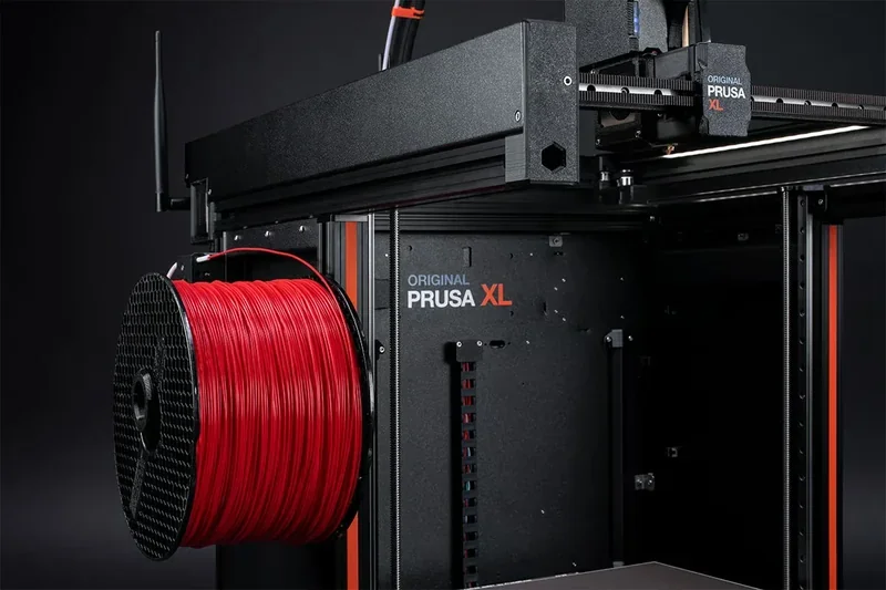 Original Prusa XL 3D printer with red filament spool, showcasing large build area and branding in a professional studio setting.