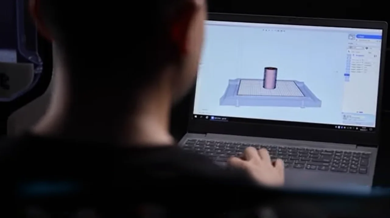 Designer creates 3D model on laptop for Qidi I-Fast printer; screen shows cylindrical part prepared for printing.