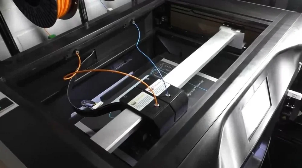 Qidi I-Fast 3D printer close-up showing internal mechanism and extruder, with colored wires and spools indicating its printing setup.