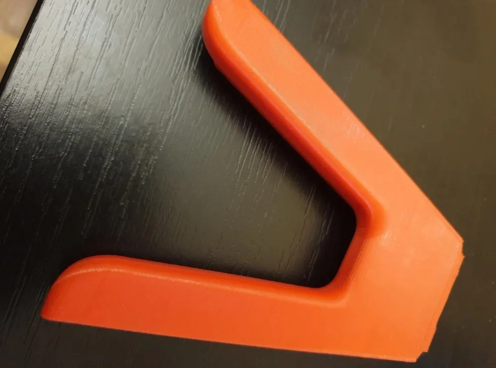 Red 3D-printed corner piece created by Qidi I-Fast on a dark wooden surface.