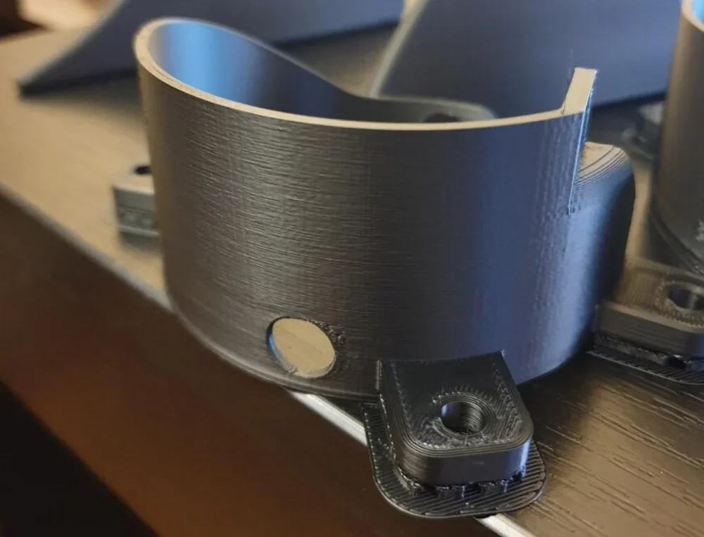 Curved black 3D-printed part created by Qidi I-Fast, with a smooth surface and precise cutouts, displayed on a wooden table.