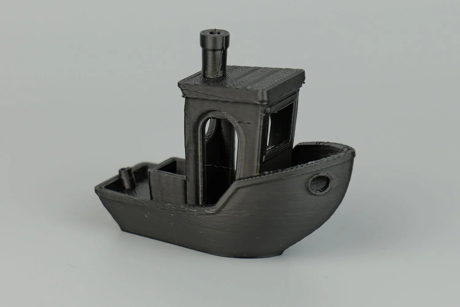 Black 3D-printed boat model created by QIDI X MAX, showcasing detailed layers and smooth finish on a gray background.