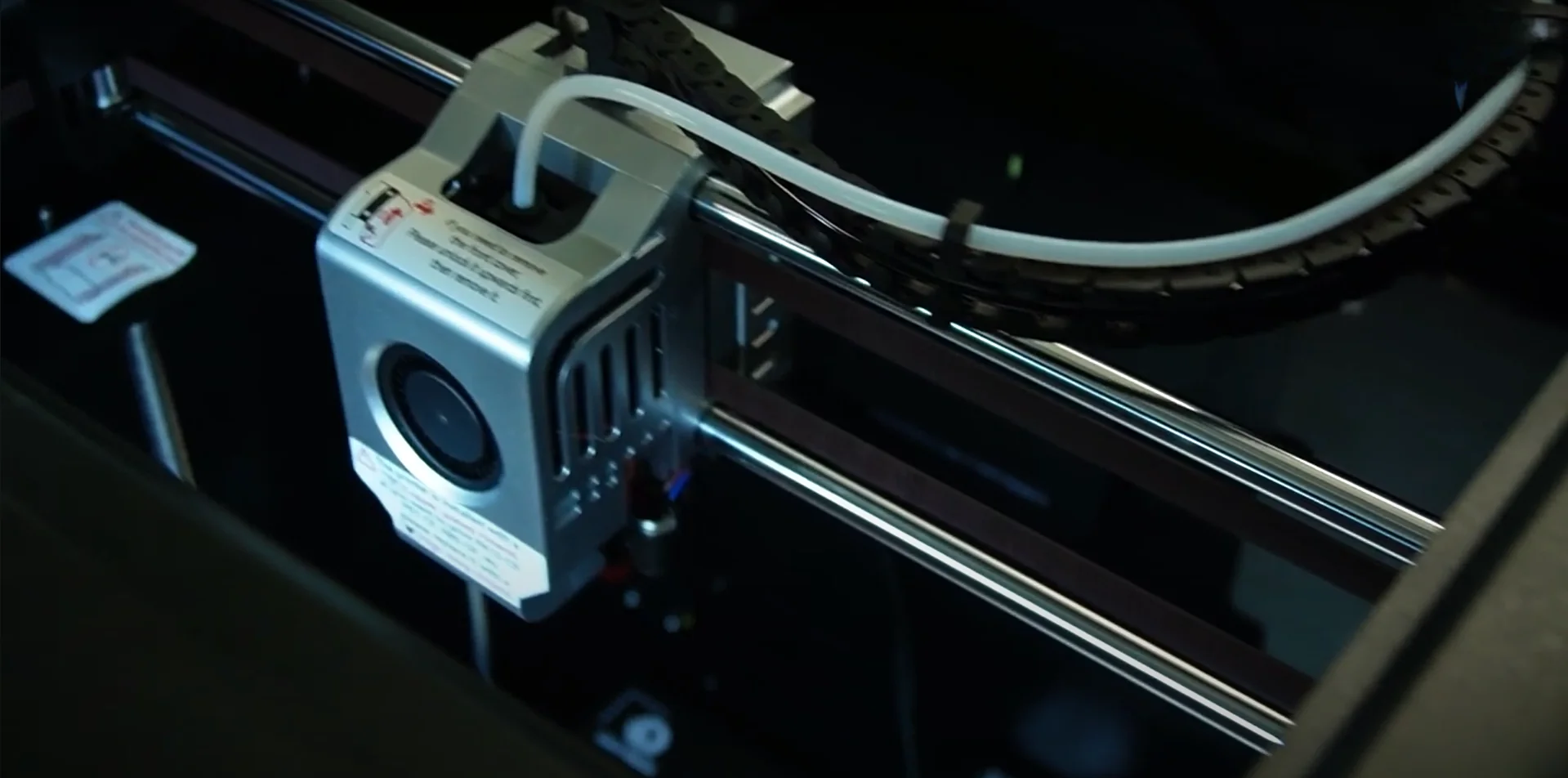 Qidi X Max 3D printer close-up showing extruder mechanism, metal frame, and cabling. Parts and components suggest precision and advanced technology.