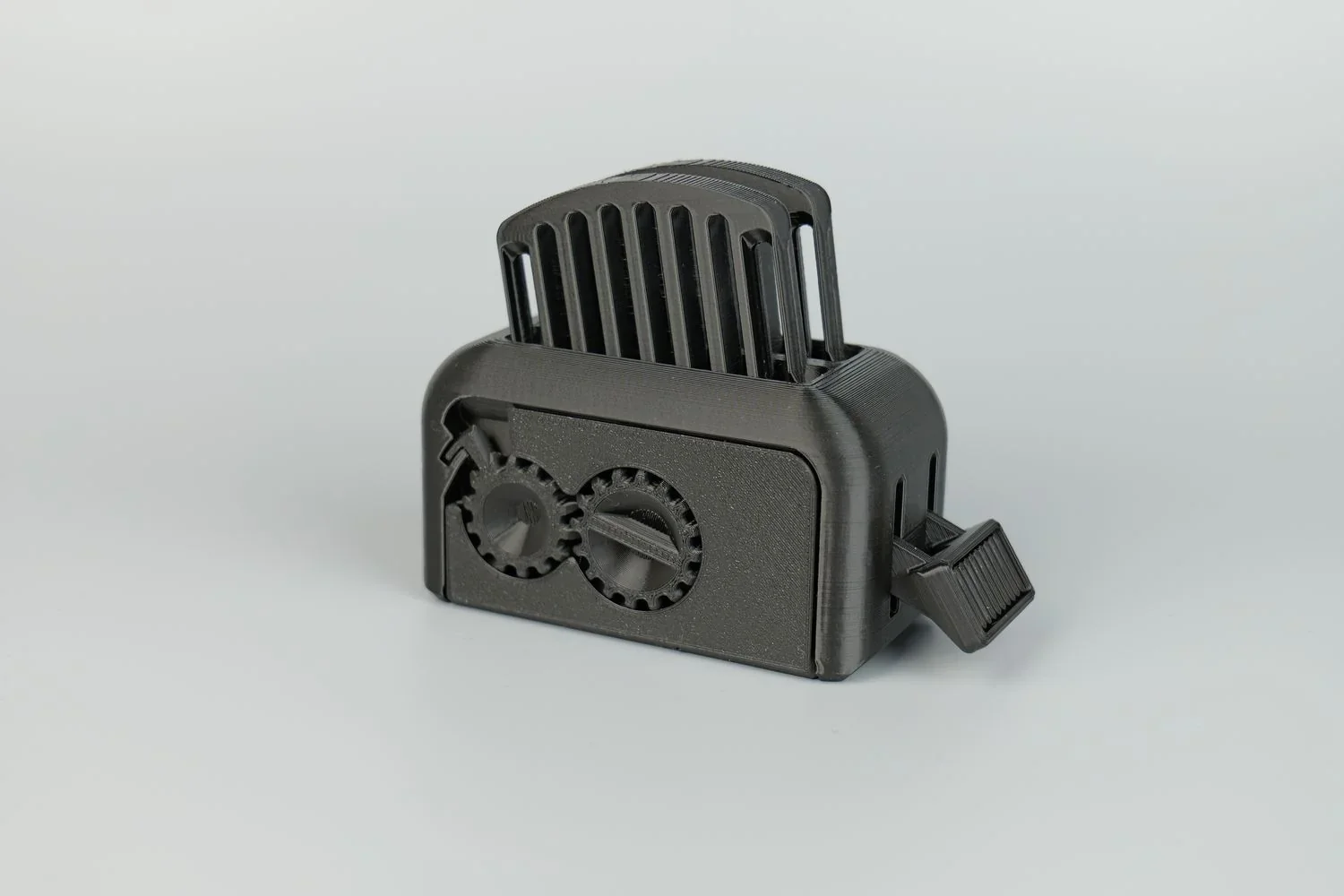 Black 3D-printed gear-based toaster model created with Qidi X Max printer on a light gray background.