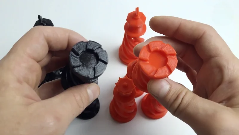 Hands holding black and red 3D-printed chess pieces, likely created by Raise3D E2, showcasing intricate design details and precise craftsmanship.