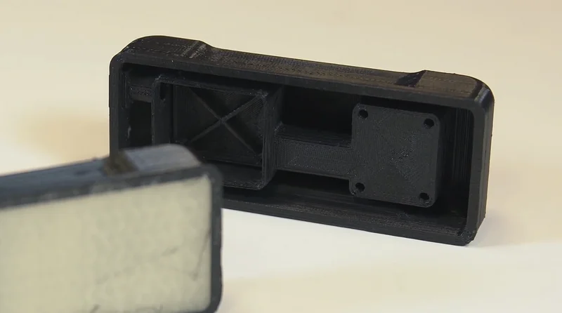 Two black 3D printed parts created by Raise3D E2, featuring geometric shapes and textured surfaces, set against a neutral background.