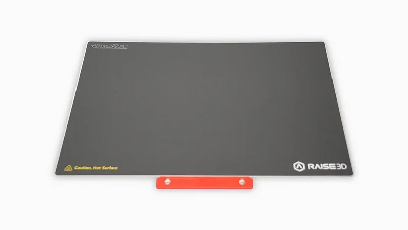 Raise3D E2 build plate with black surface, orange handle, logo, and "Caution, Hot Surface" text.