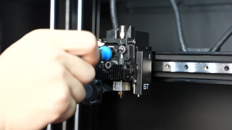 Hand adjusting nozzle gears on Raise3D E2CF 3D printer extruder in a black casing, showcasing precision components and wiring.