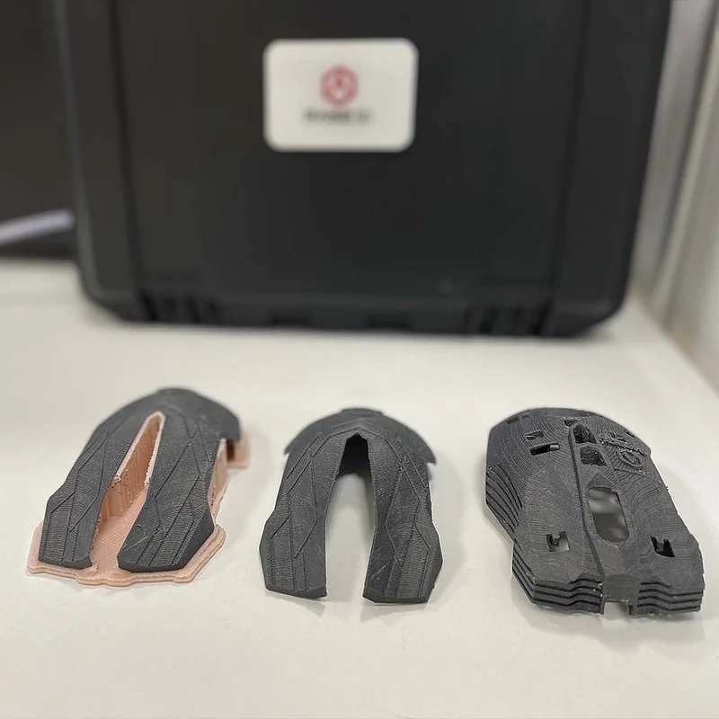 Raise3D E2CF 3D printer with three carbon fiber parts on display, showcasing detailed design and precision manufacturing.