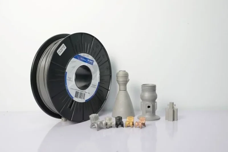 3D printed metal parts and filament spool by Raise3D Metalfuse displayed on white surface, showcasing a variety of printed metal components.