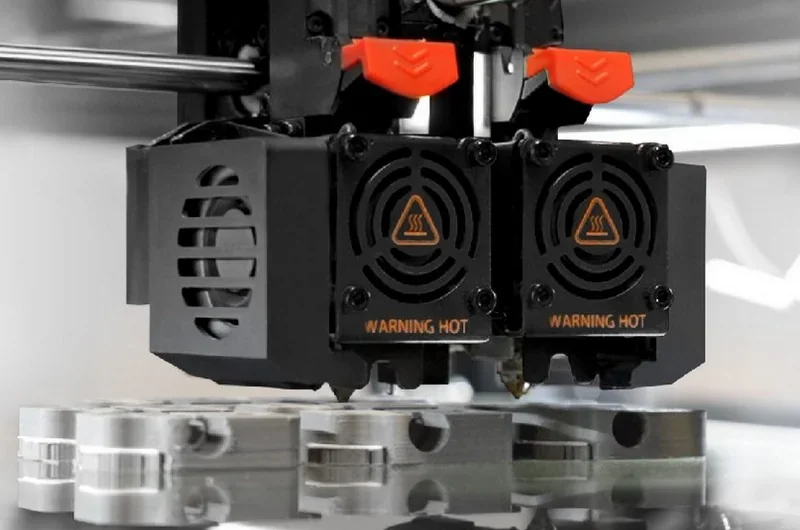 Raise3D MetalFuse dual extruder close-up with heated nozzles above metallic parts, showcasing advanced 3D printing technology.