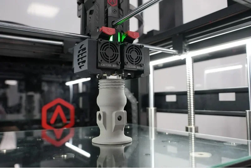 Raise3D MetalFuse 3D printer creating a detailed metal part with branding visible in a well-lit setting.