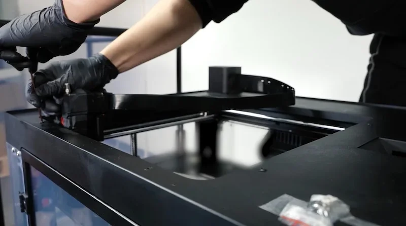 Person adjusting Raise3D MetalFuse 3D printer, showcasing precision engineering and industrial build, with potential metal parts on the desk.