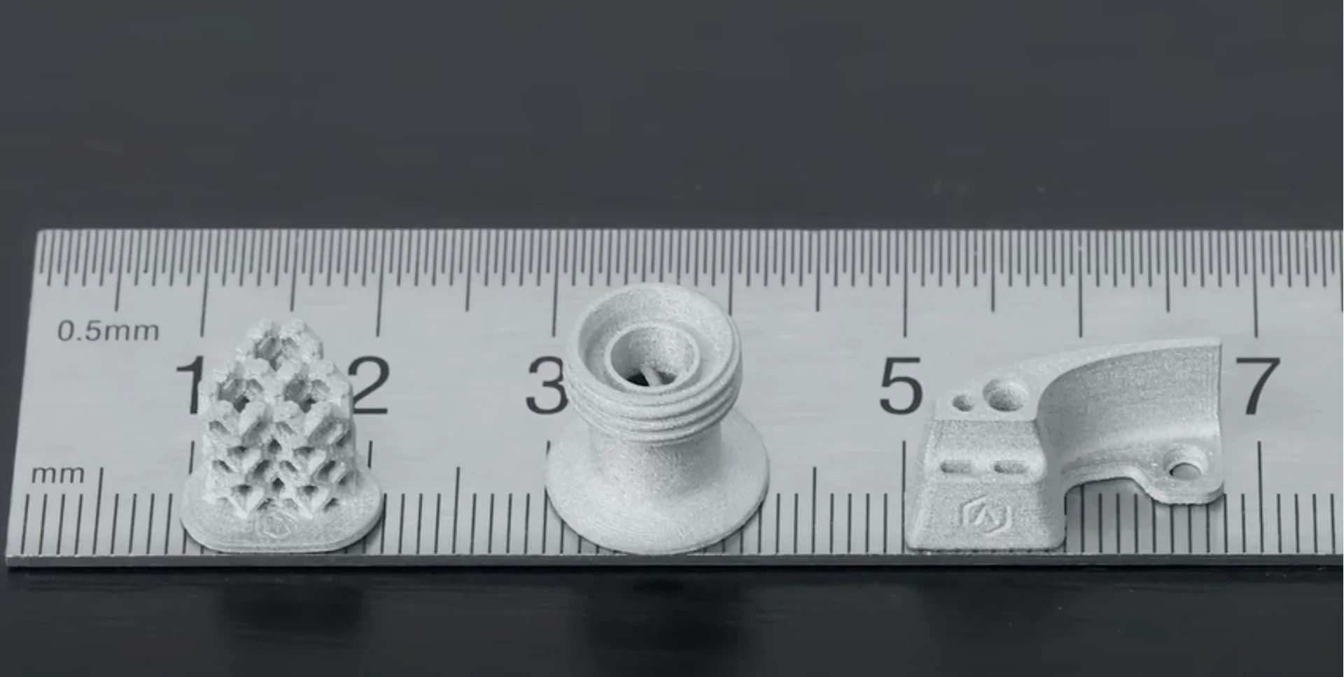 3D printed metal parts made by Raise3D MetalFuse displayed on a ruler for scale, showcasing intricate designs and precision detailing.