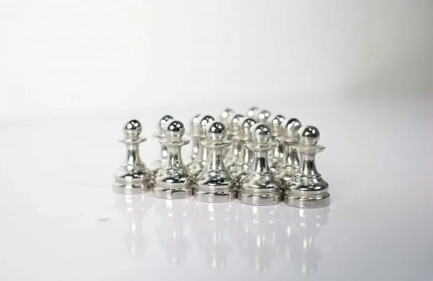 Silver chess pawns 3D printed using Raise3D MetalFuse, arranged in a reflective setting, showcasing precision and metallic finish.