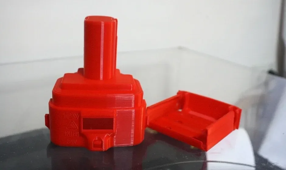 Red 3D-printed object and open box, precision-crafted by raise3d pro2 plus, displayed on a flat surface with visible text details.