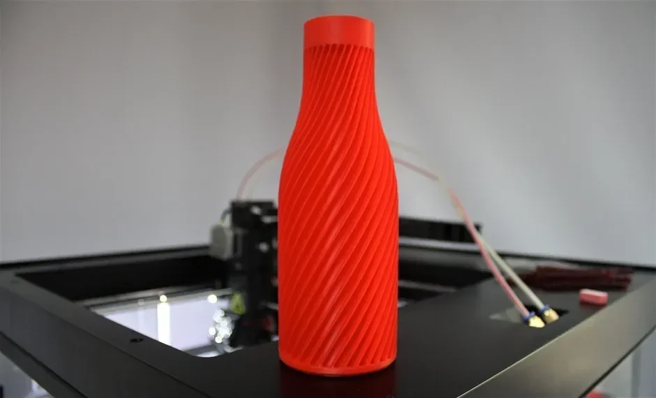 Red spiral vase 3D-printed by Raise3D Pro2 Plus on a black platform, showcasing intricate design and precise manufacturing capabilities.