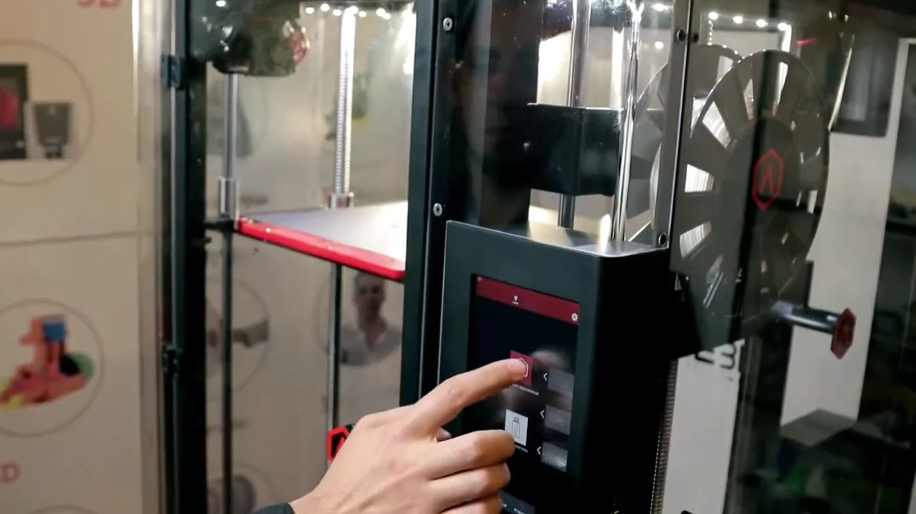 Raise3D Pro2 Plus with touchscreen interface, large printing chamber, spool holder, and sample 3D-printed parts on display in a workshop setting.