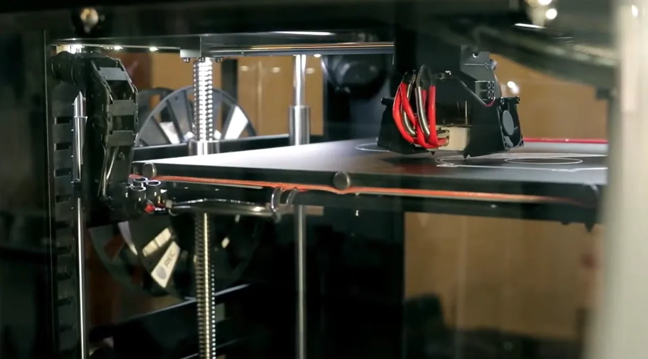 Raise3D Pro2 Plus 3D printer in action, featuring mechanical components and a build plate, with printed parts partially visible inside the enclosure.