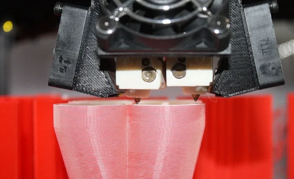 Raise3D Pro2 Plus 3D printer nozzle printing a red object, showcasing precision and detail in a workshop setting.