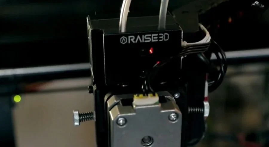 Raise3D Pro2 Plus with visible branding, focus on extruder assembly, wires, and components, likely fabricating a part using advanced 3D printing technology.